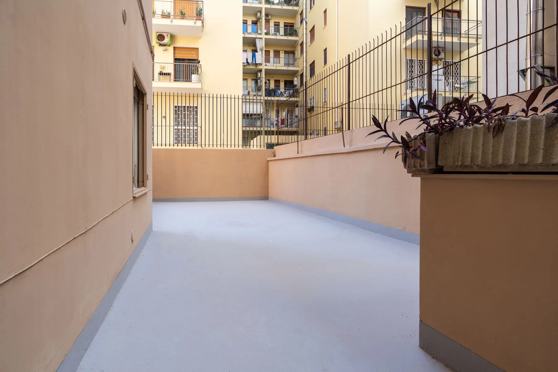 A paved outdoor terrace bordered by apartment buildings and planted planters.