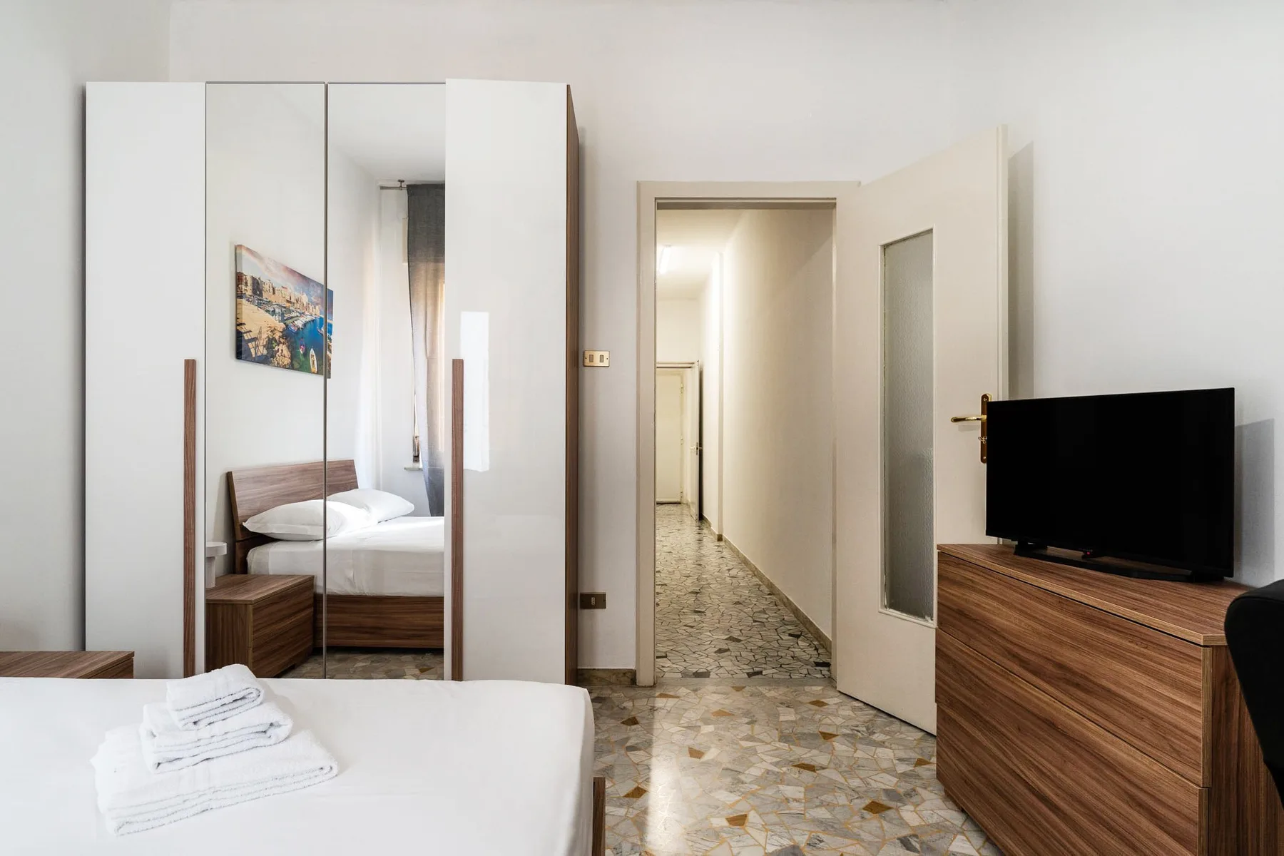 A bedroom with a bed, mirrored wardrobe, and a doorway opening onto a hallway.