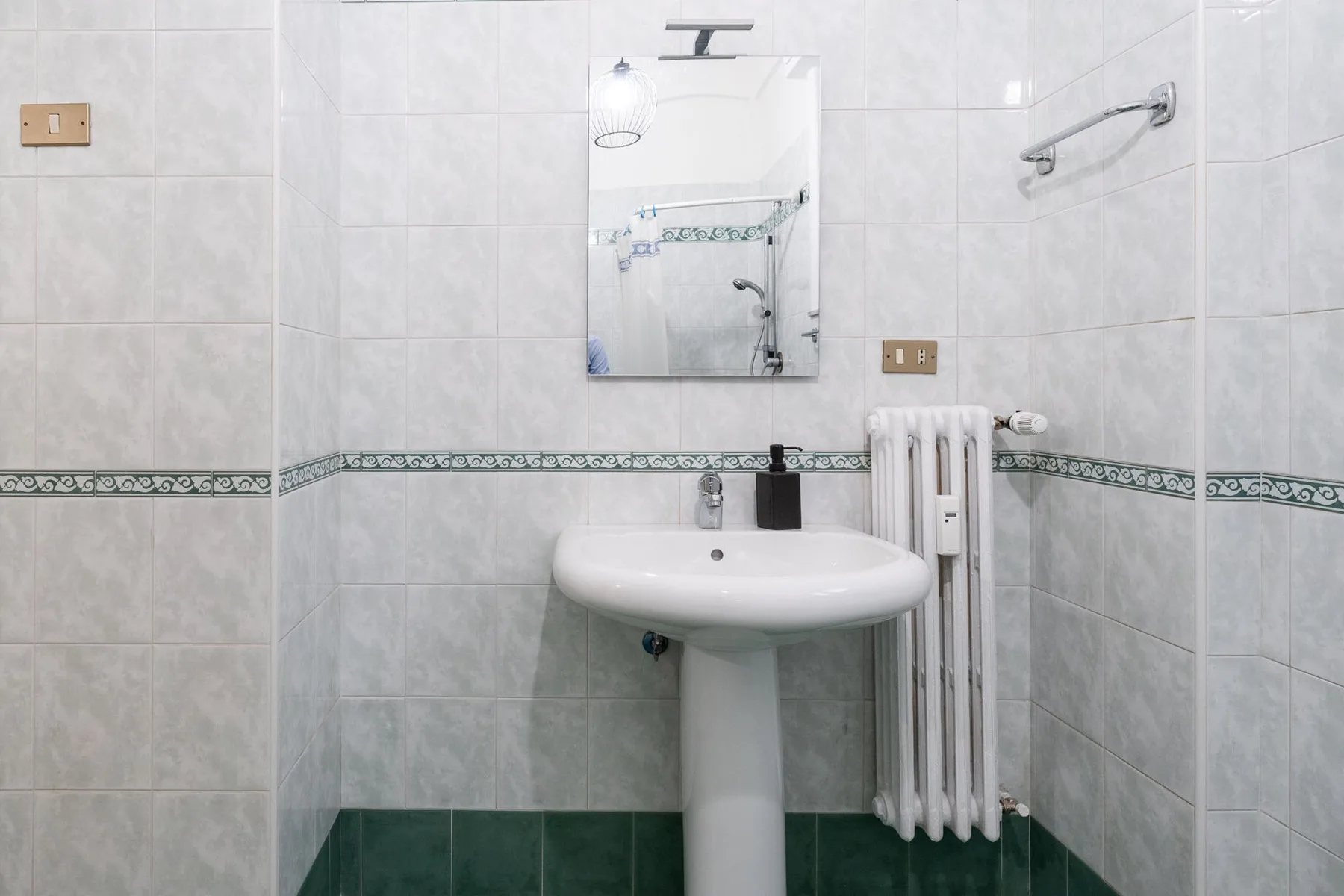 A tiled bathroom with a pedestal sink, mirror, and towel radiator.