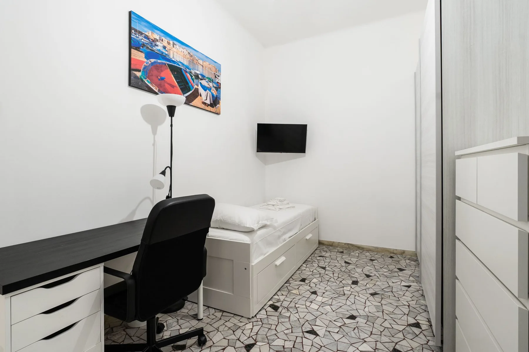 Un dormitorio compacto con una cama individual, escritorio y silla negra.