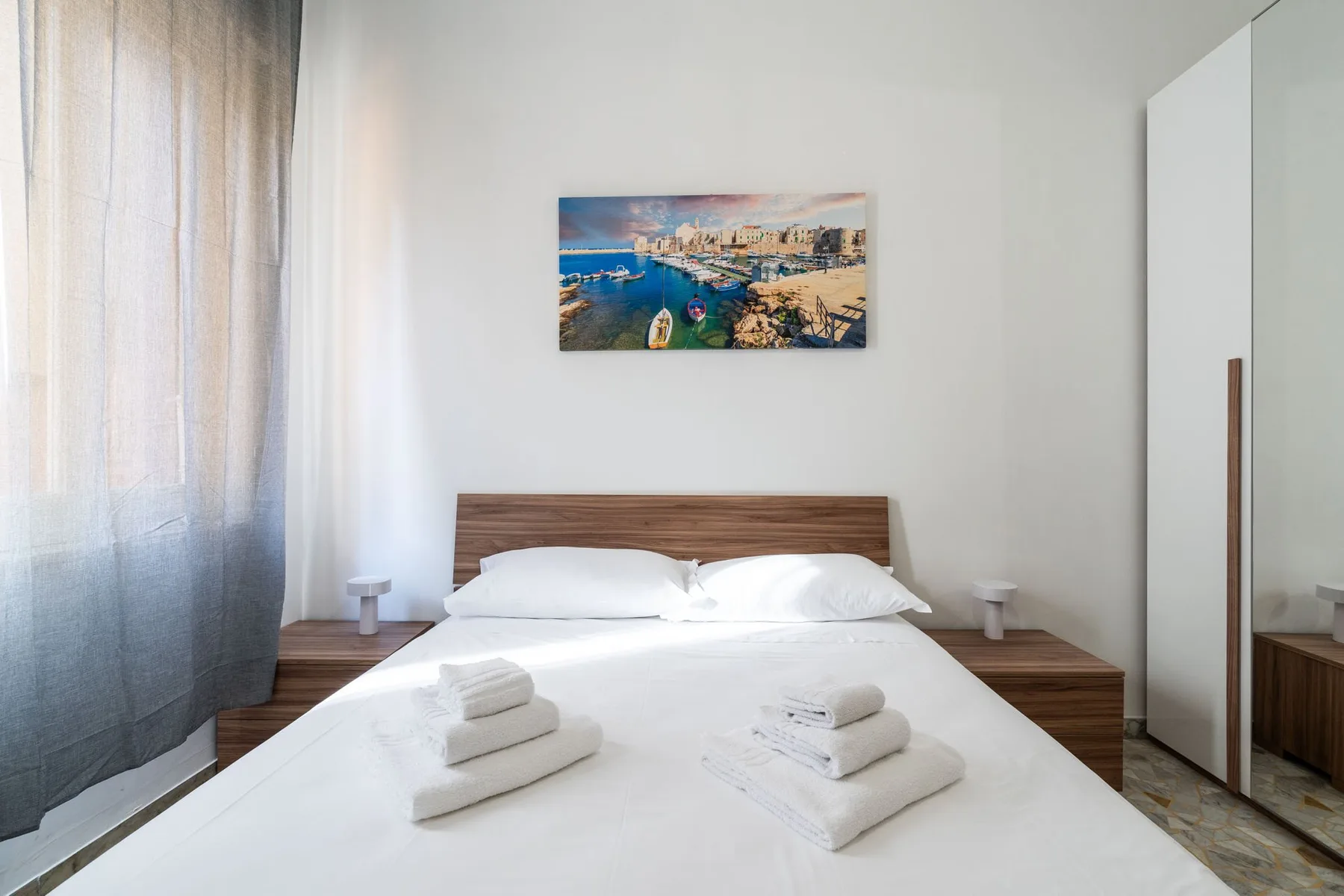 A bright bedroom with a double bed and a framed coastal picture above the headboard.