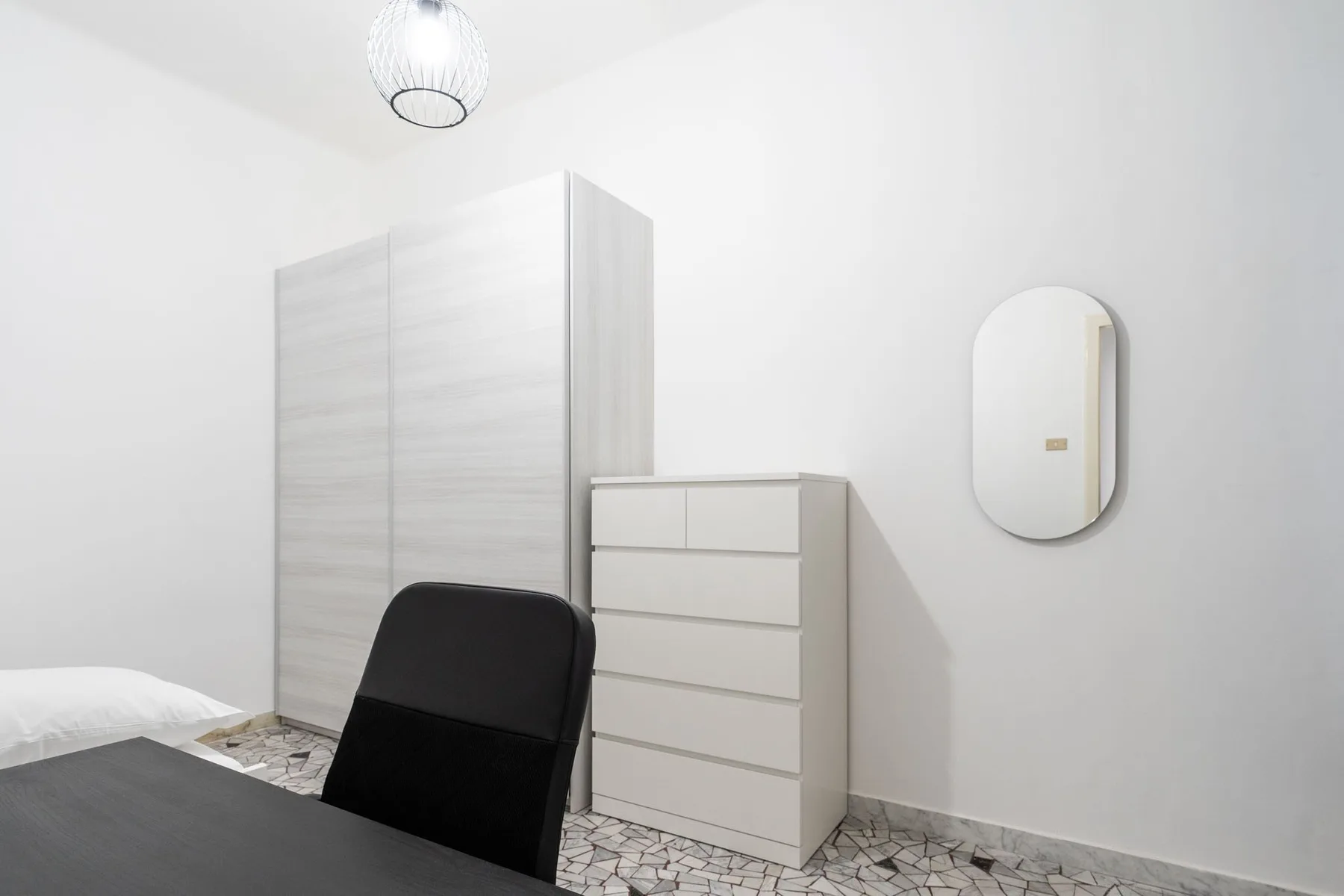 A bright bedroom with a wardrobe, chest of drawers, and dark seating.