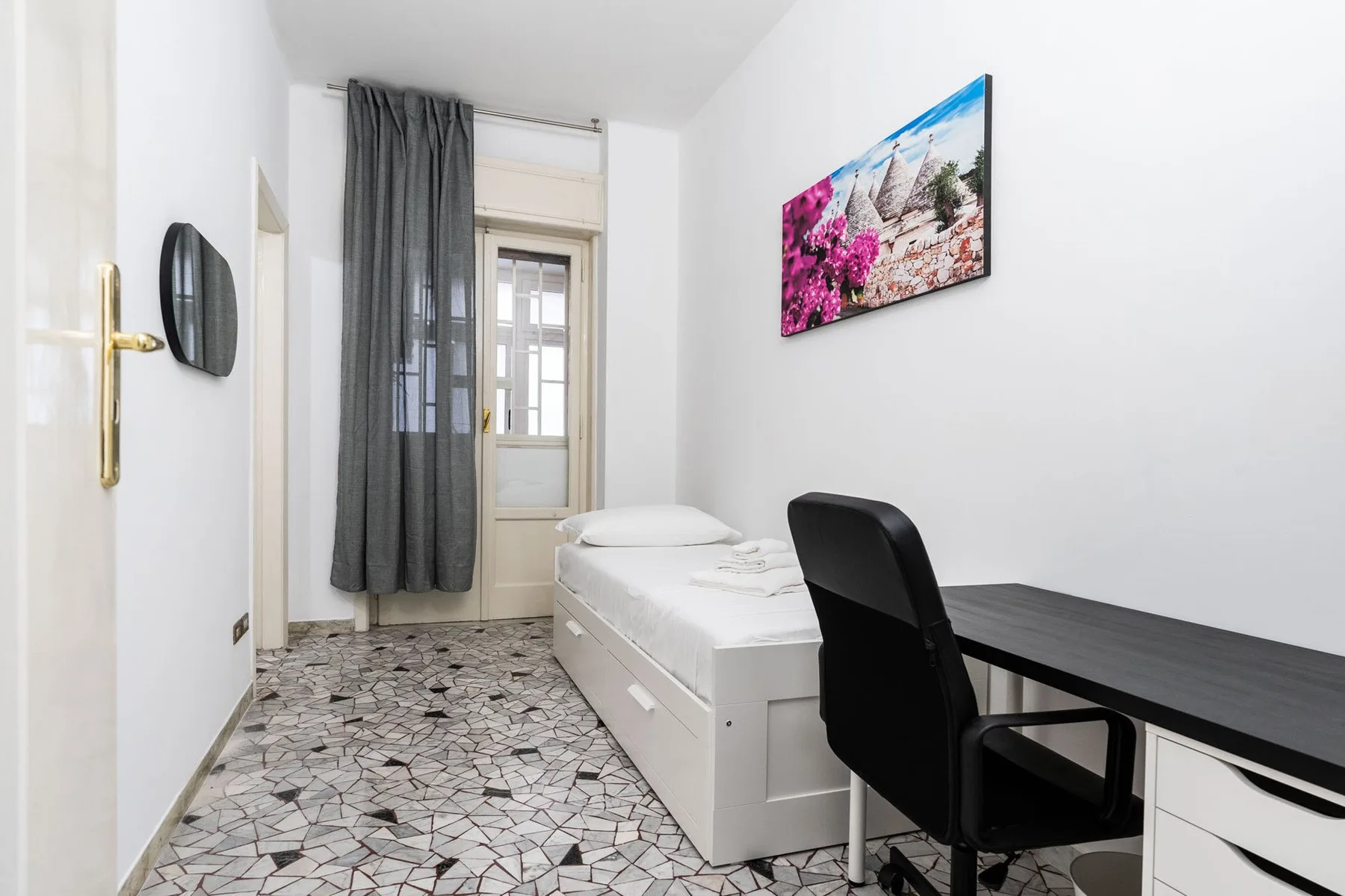 A compact bedroom with a single bed, desk, and dark curtains.