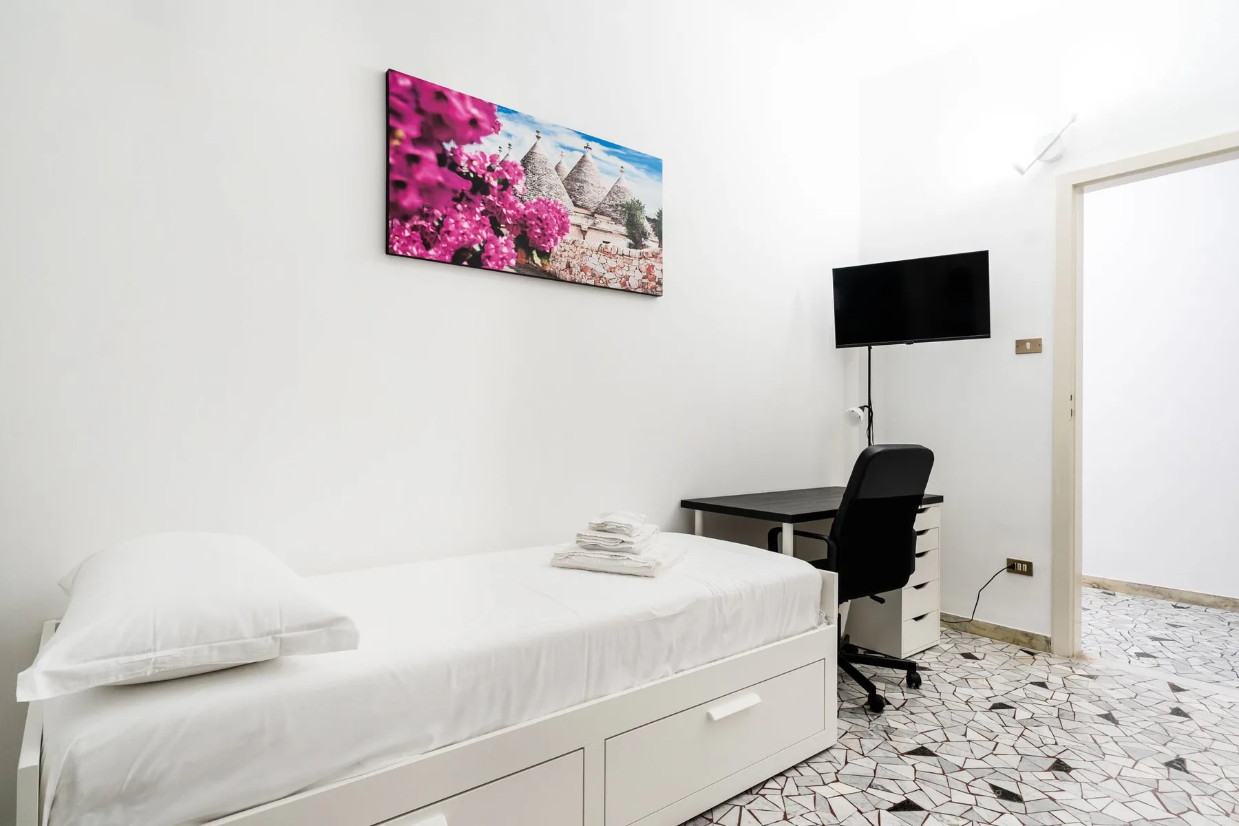 Un dormitorio con una cama individual y un escritorio bajo un televisor montado en la pared.