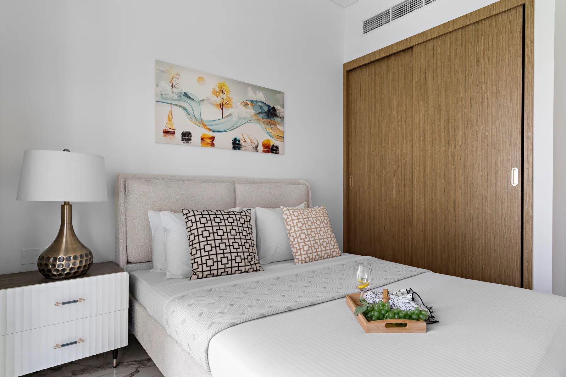 A bedroom with a neatly made bed, patterned cushions, and artwork above the headboard.