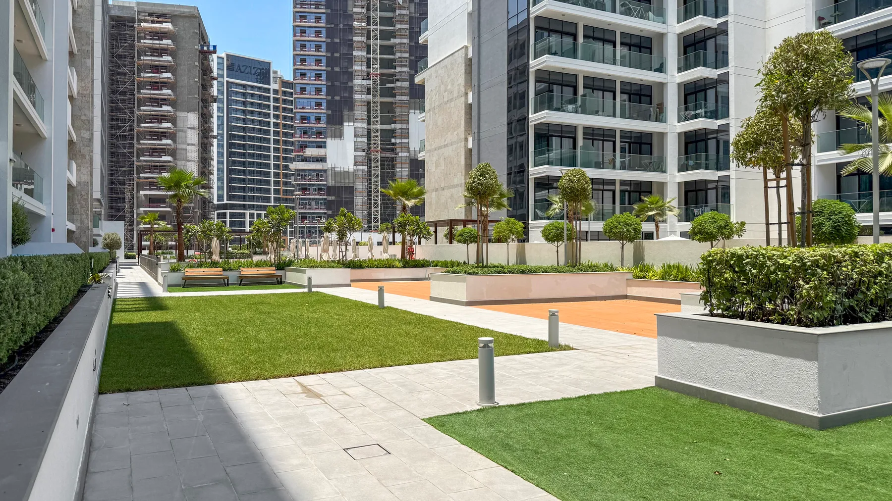 An outdoor courtyard with paved walkways, green lawn, planters, and surrounding high-rise buildings.