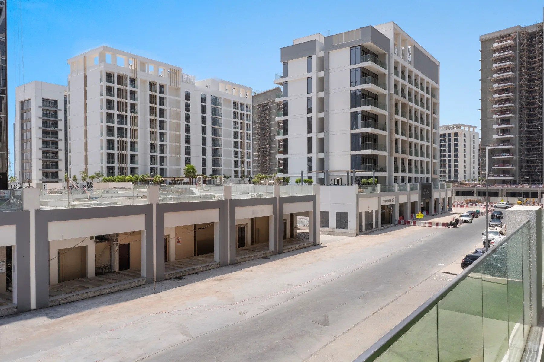 Modern apartment buildings line a paved street under a clear blue sky.