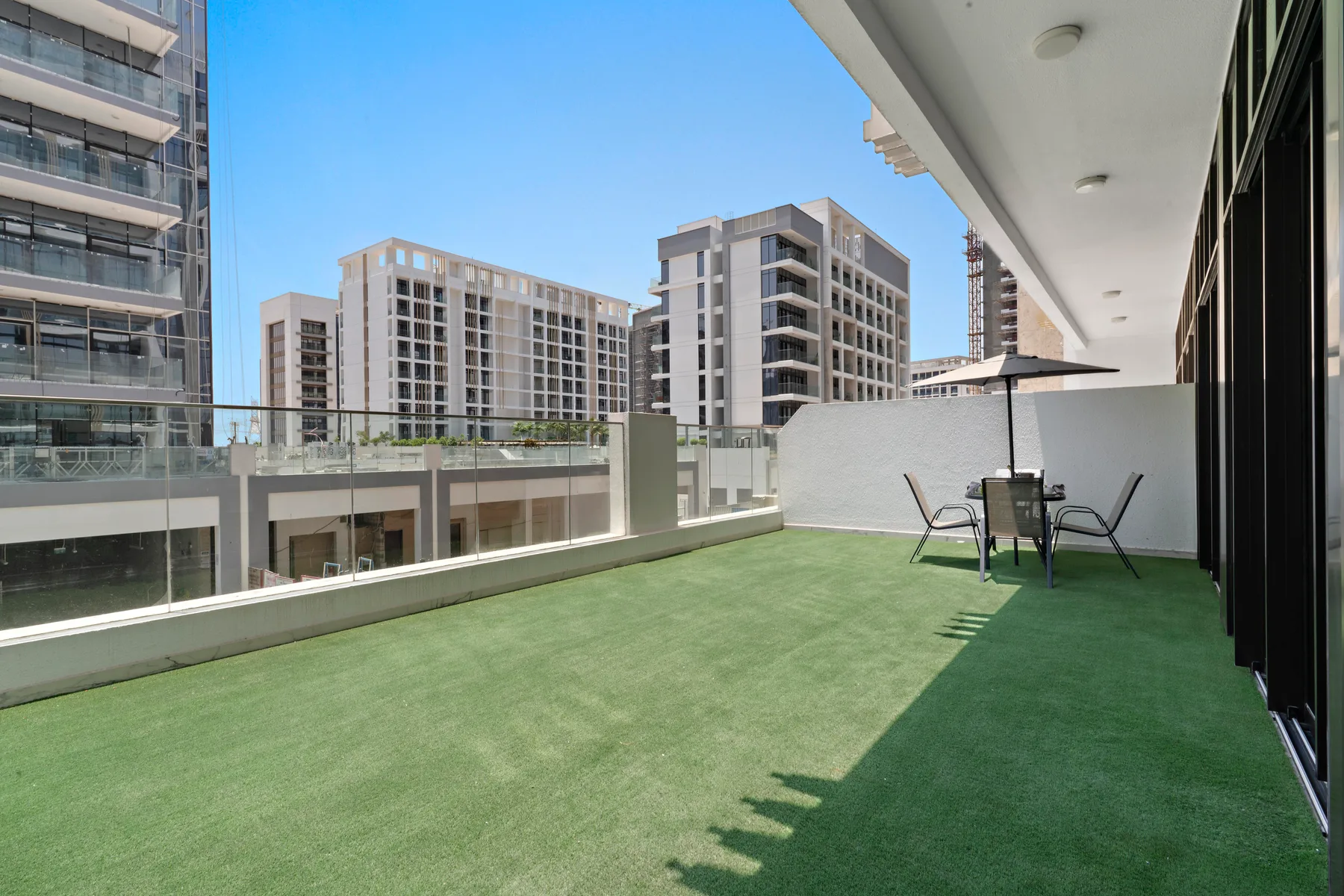 A terrace with green flooring, outdoor seating, and views of nearby buildings.
