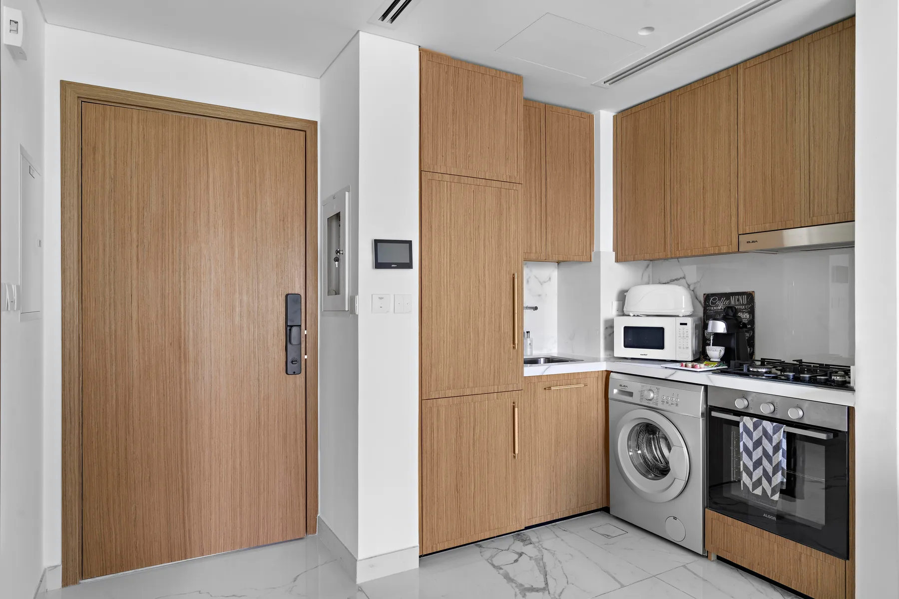 A modern kitchen with wood cabinets, a washer, and a stove.