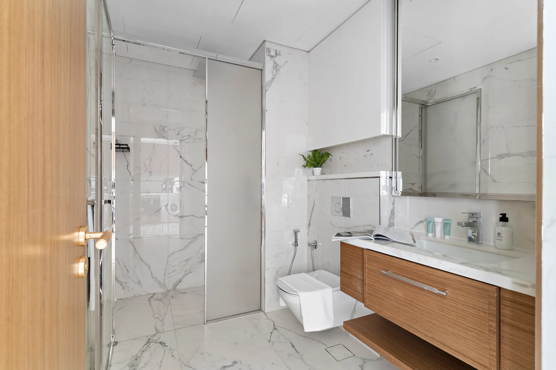 A bright bathroom with a glass shower, toilet, and wood vanity.