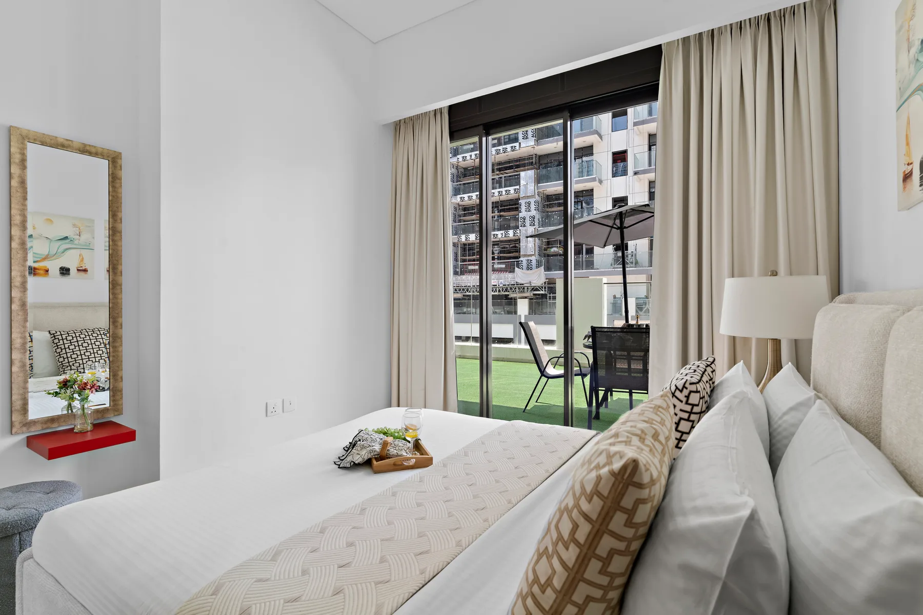 A bright bedroom with a neatly made bed beside glass doors opening onto a balcony.