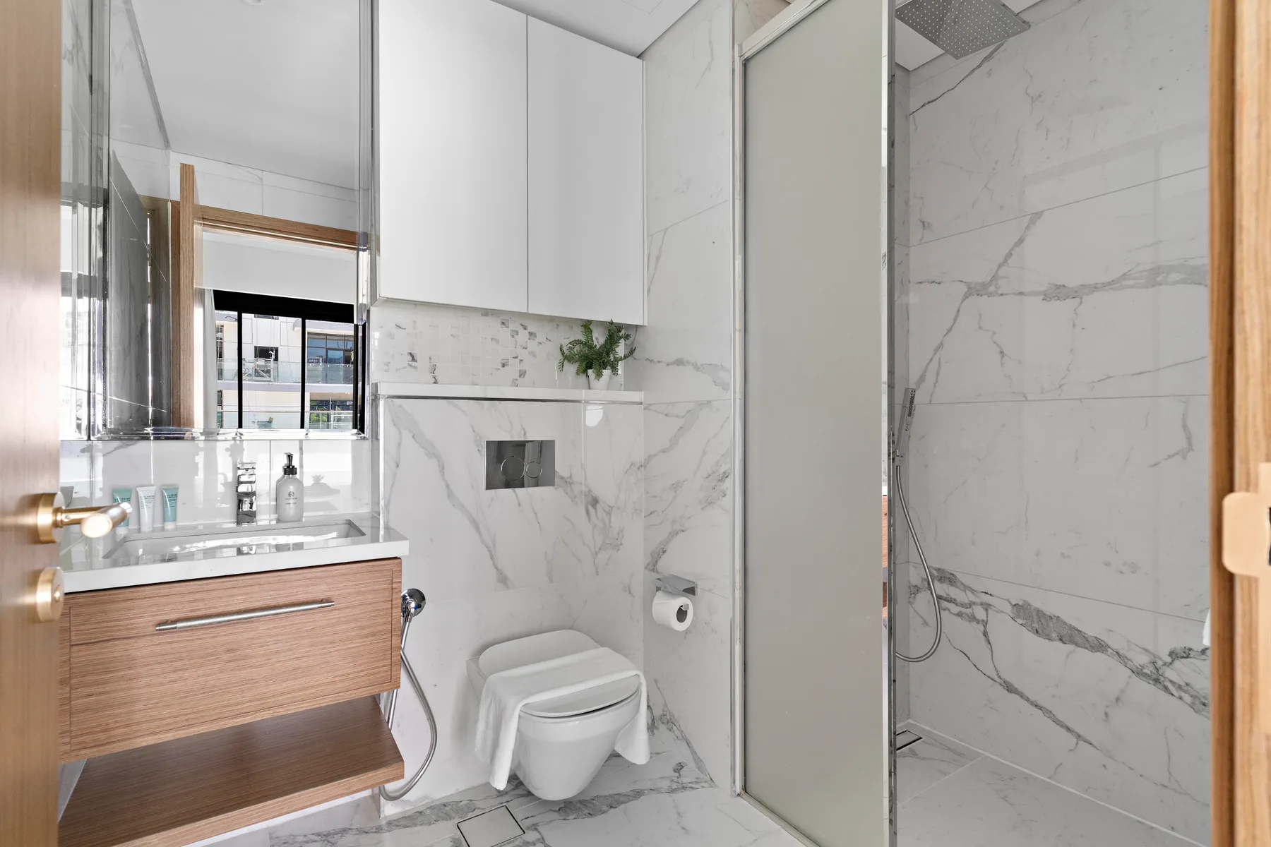 A bright bathroom with a vanity, toilet, and glass-enclosed shower.