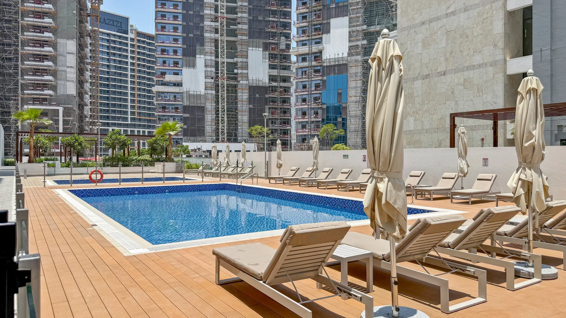 An outdoor swimming pool is surrounded by lounge seating and high-rise buildings.