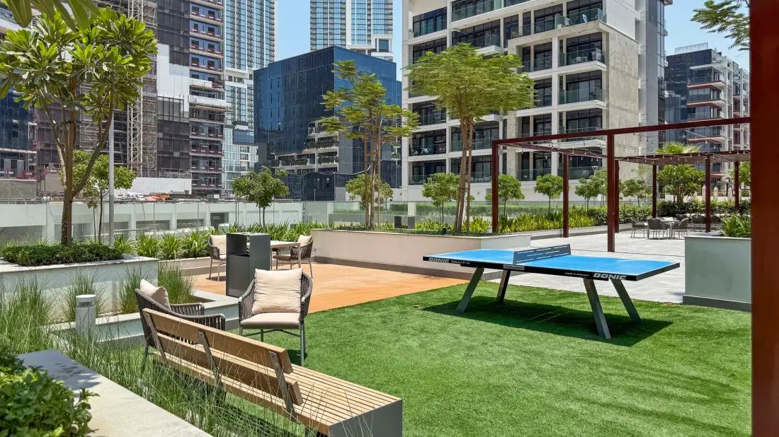 An outdoor recreation area features a ping-pong table, seating, and landscaped greenery.