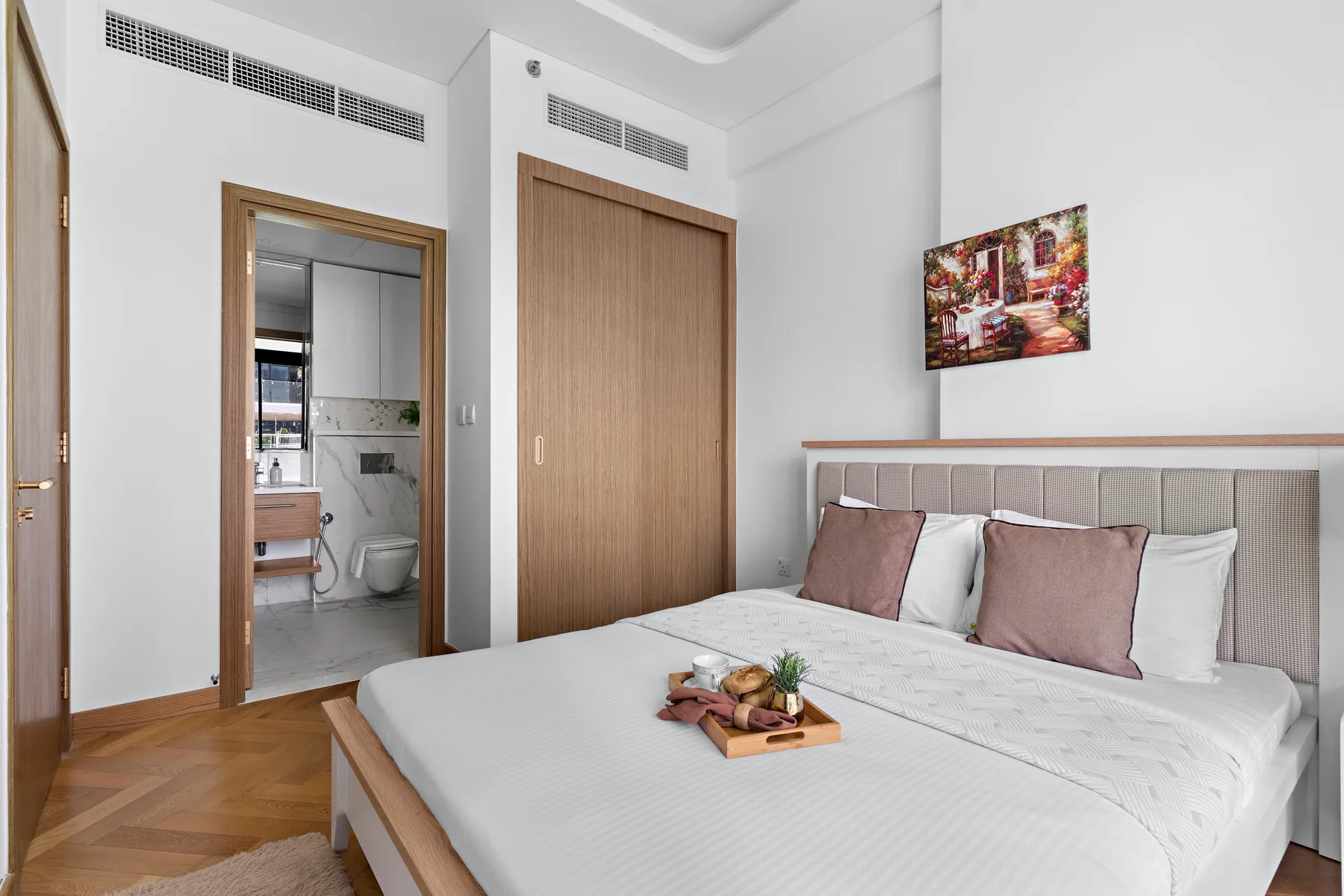 A bright bedroom with a neatly made bed and an open doorway to the bathroom.
