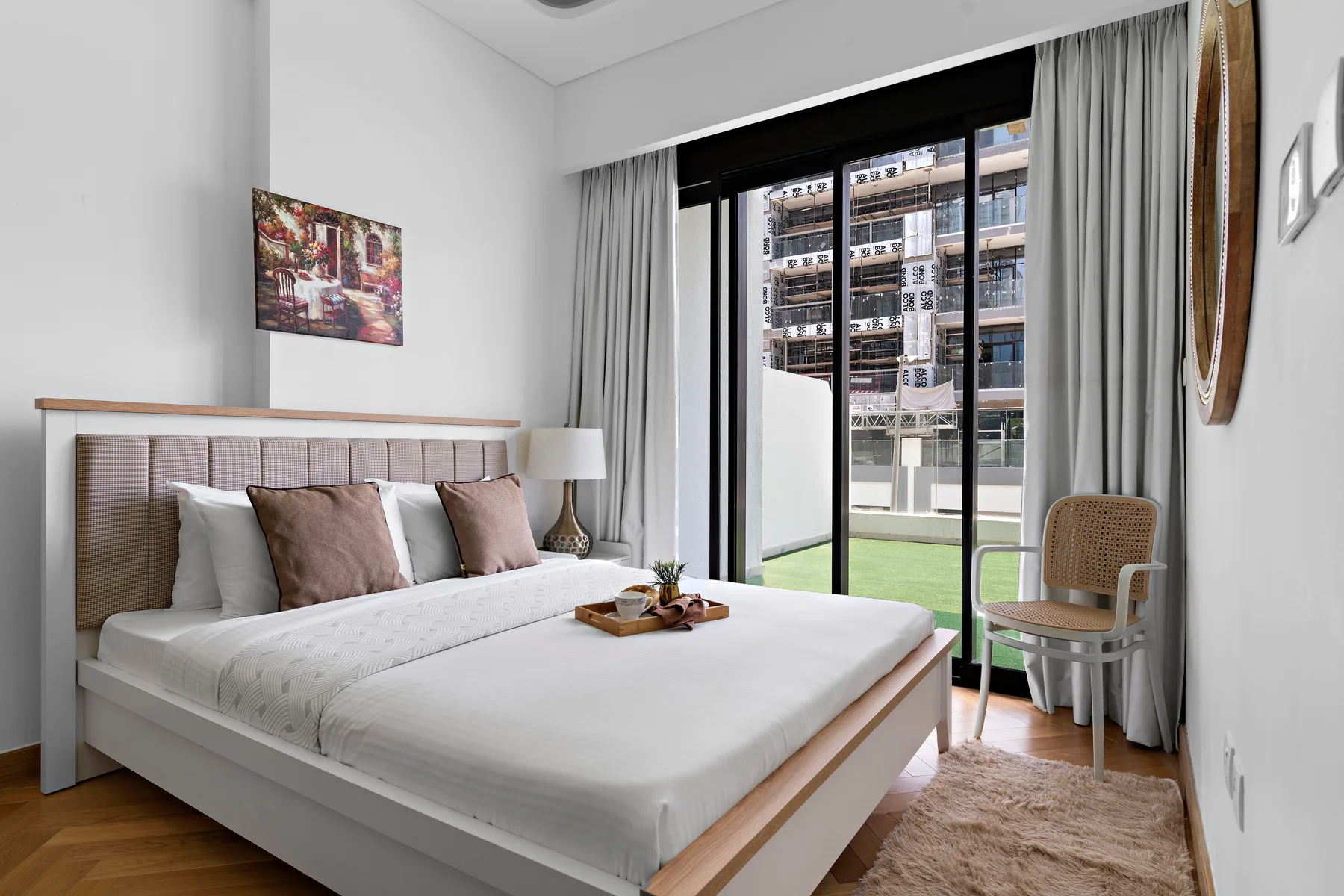 A bedroom with a neatly made bed, bedside lamp, and large windows.