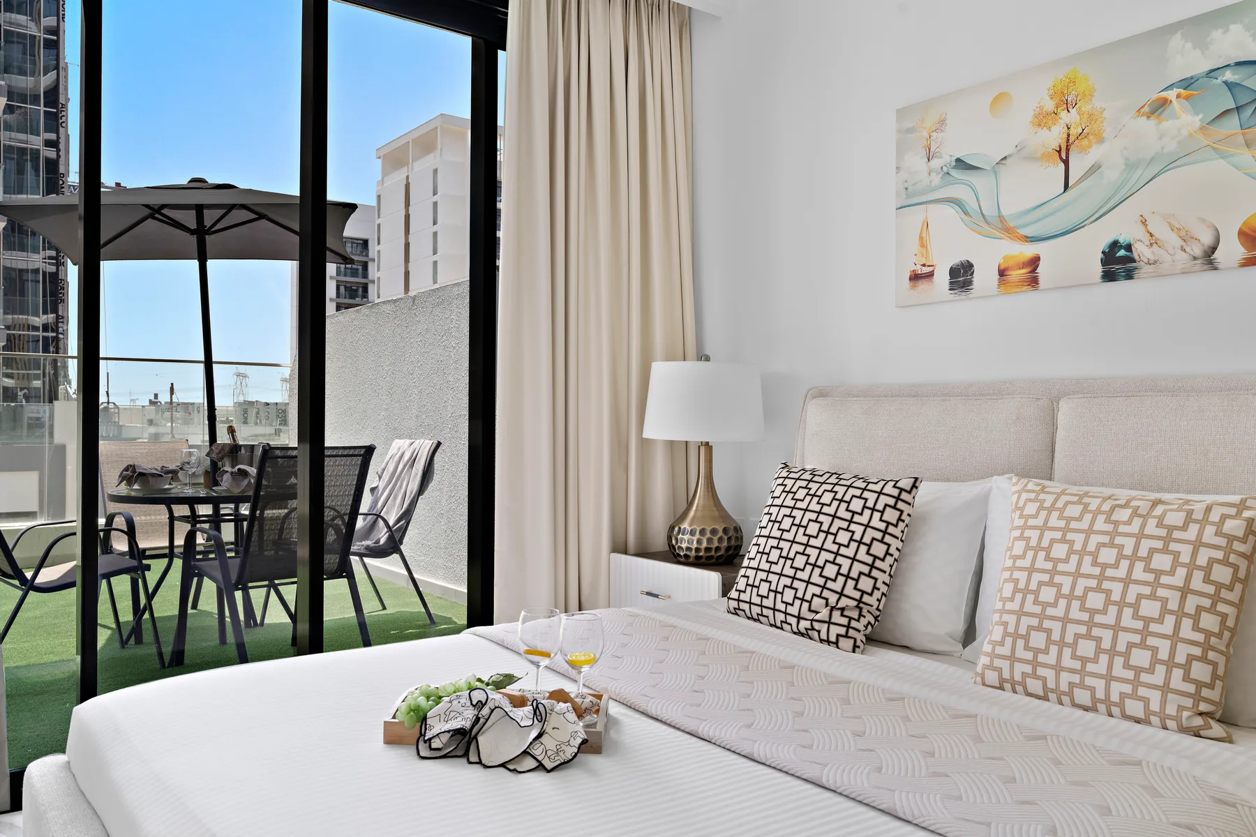 A bedroom with a bed beside large windows overlooking a furnished patio.