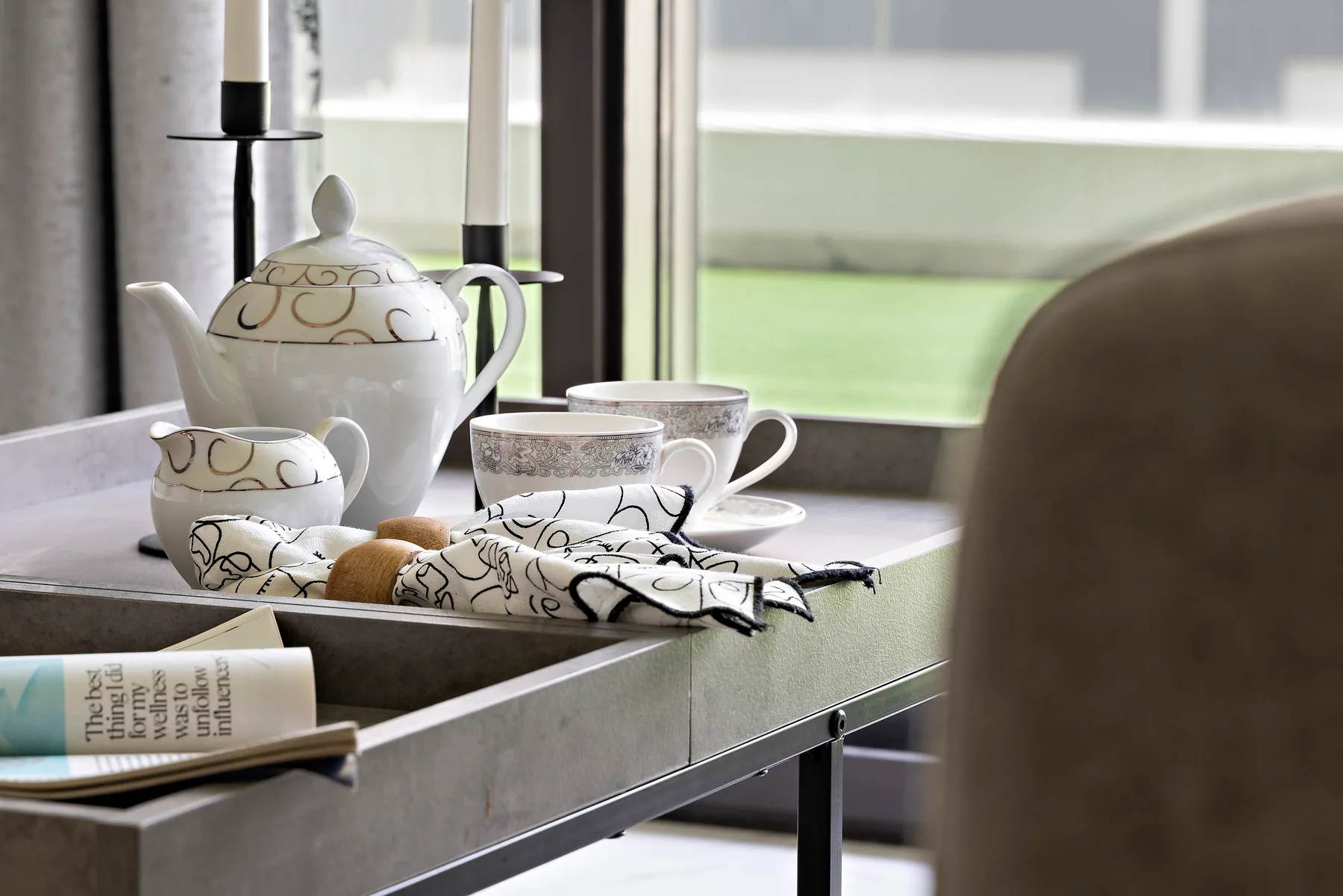 A tea service sits on a table beside a bright window.