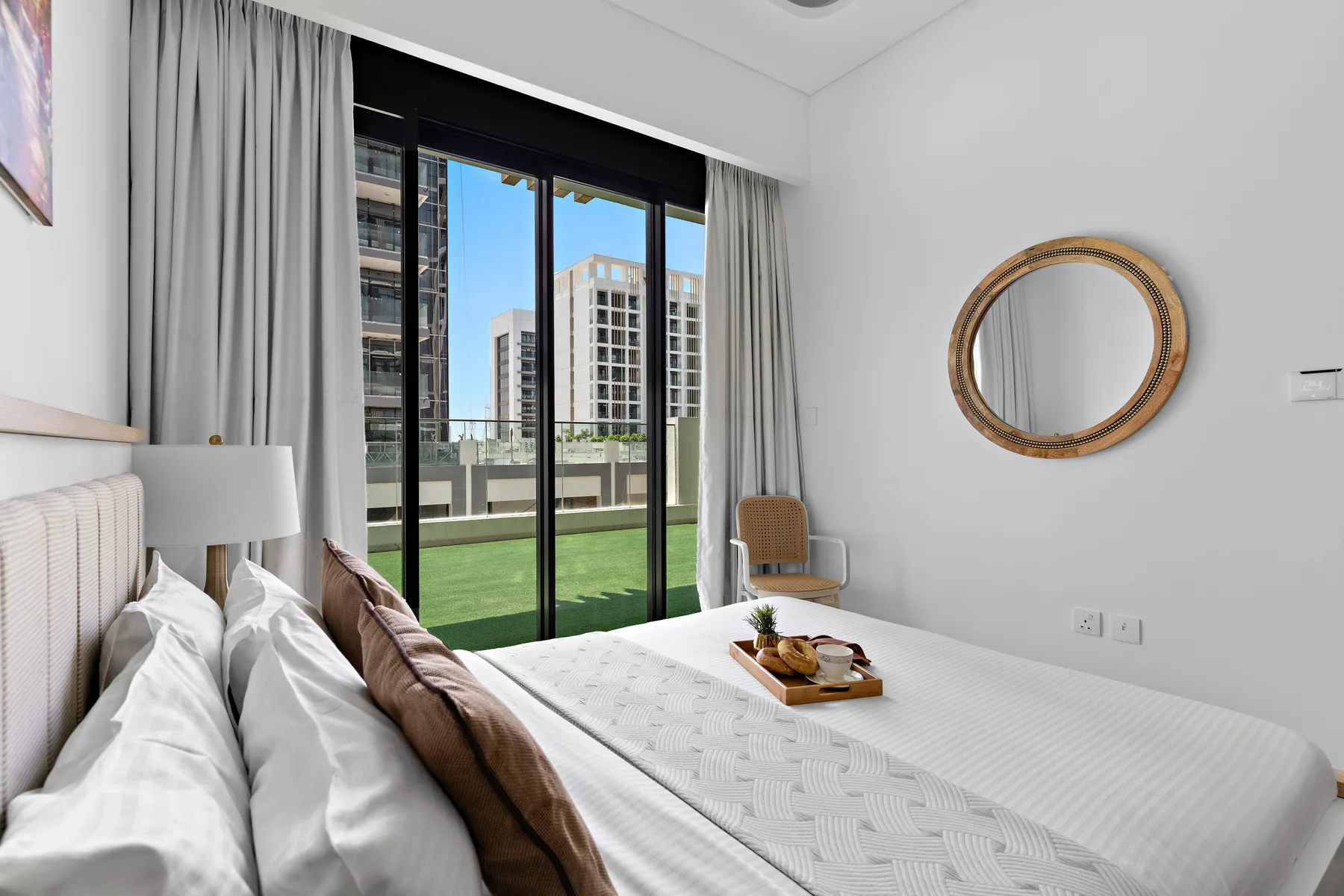 A bright bedroom with a neatly made bed and sliding glass doors opening onto a balcony.