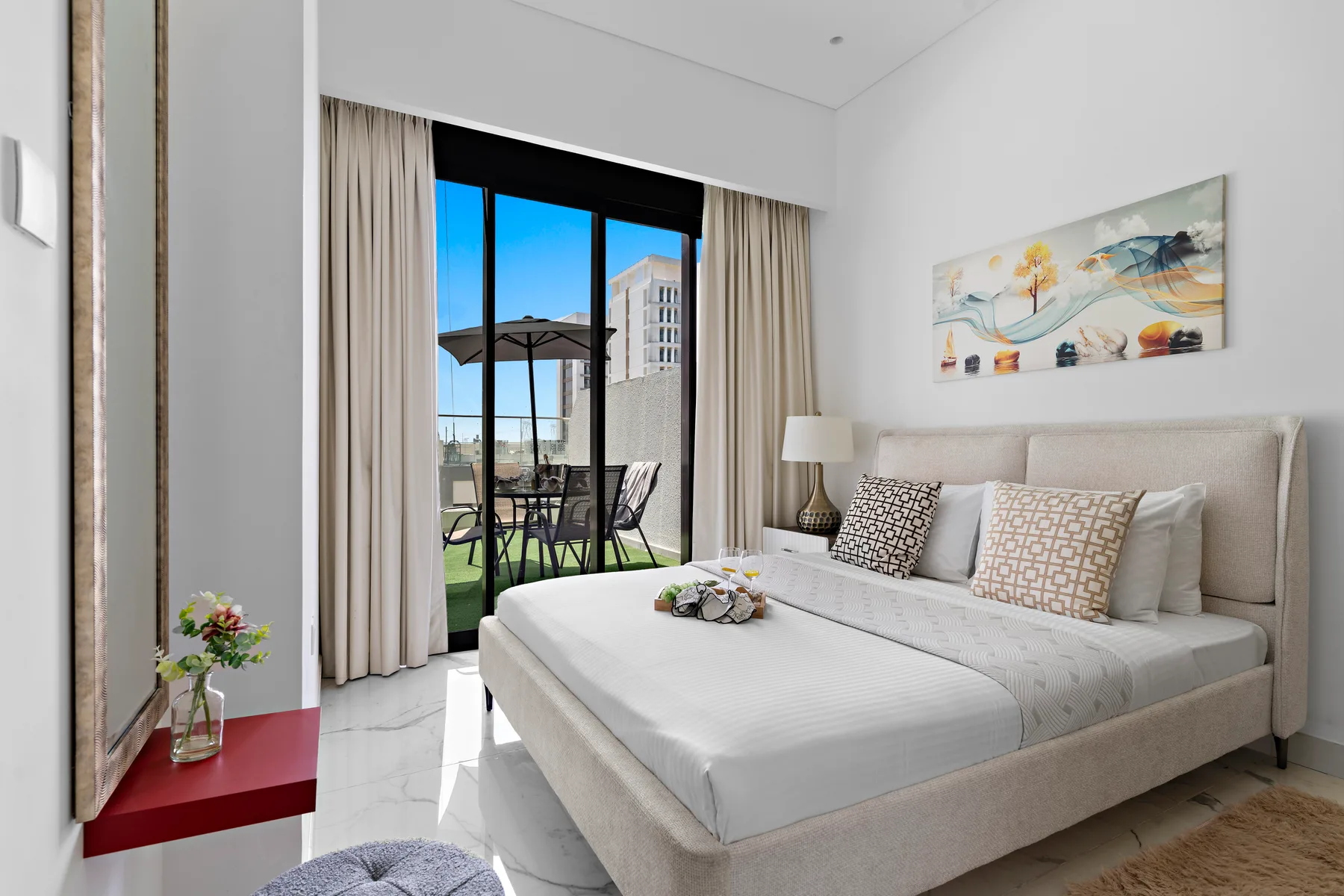 A bright bedroom with a neatly made bed and glass doors opening onto a balcony.