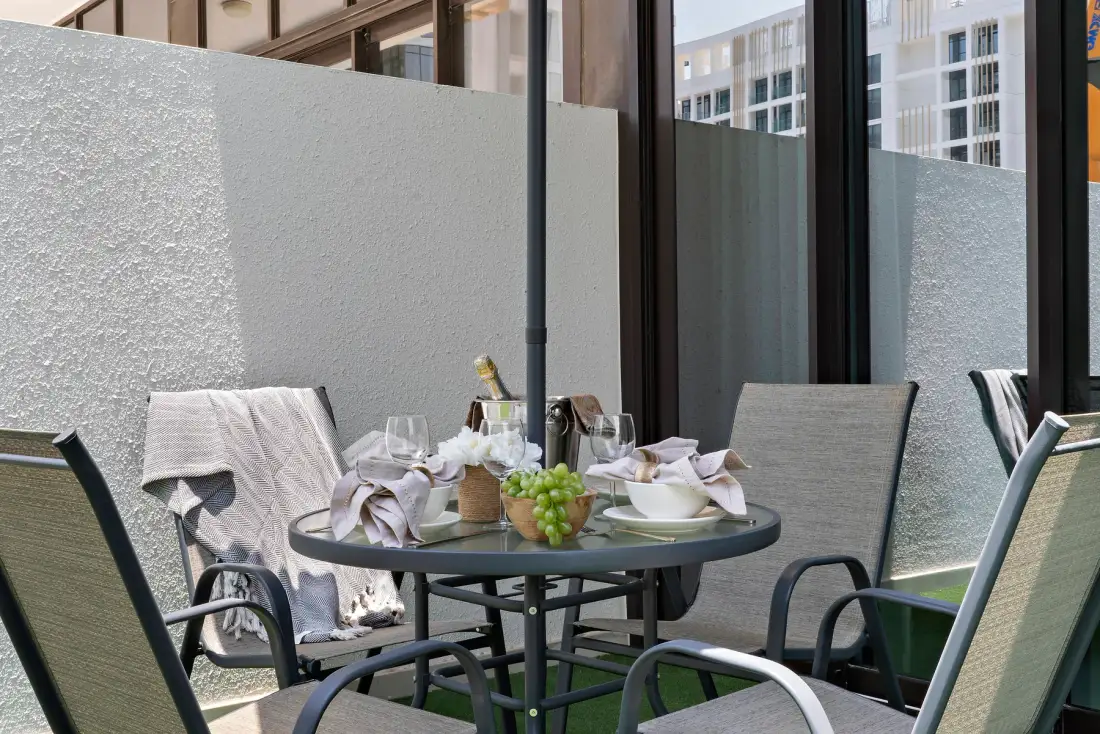 An outdoor dining area with a table set with dishes beside large windows.