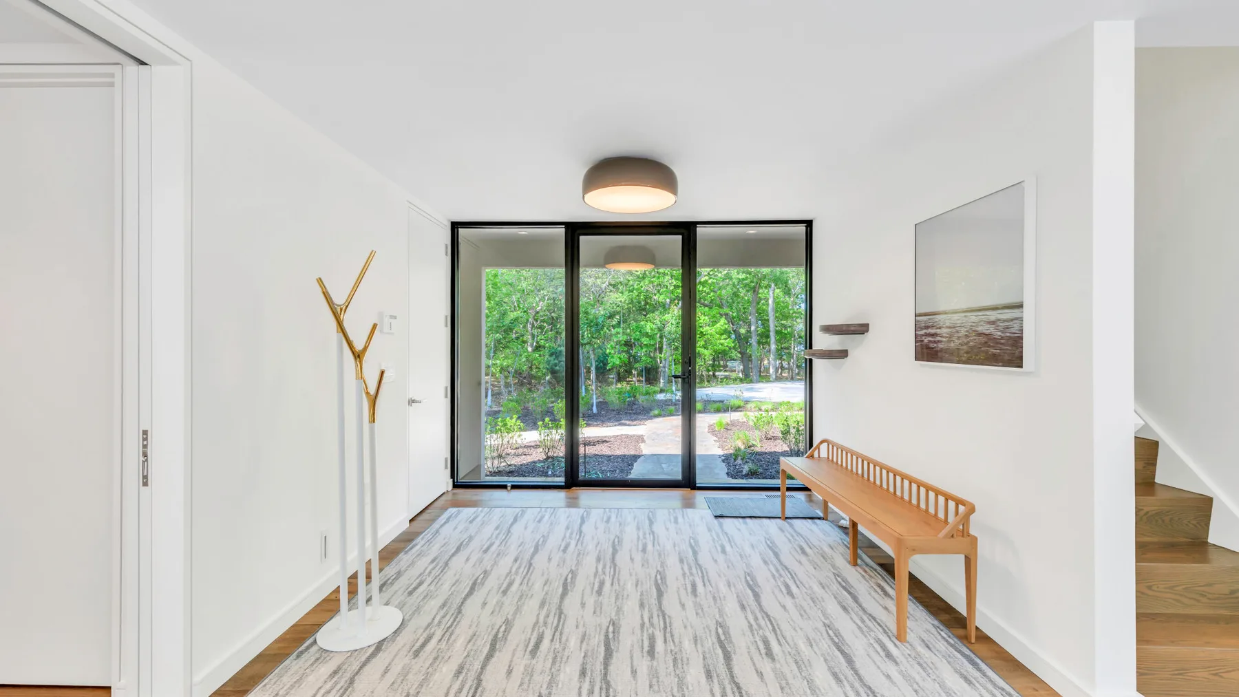 Una habitación luminosa con un banco de madera junto a grandes puertas de vidrio con vista a la vegetación.