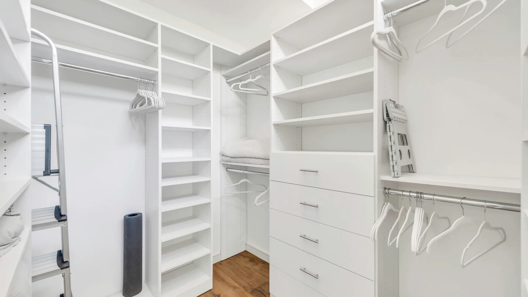 Un vestidor con estantes blancos, cajones y barras para colgar ropa.