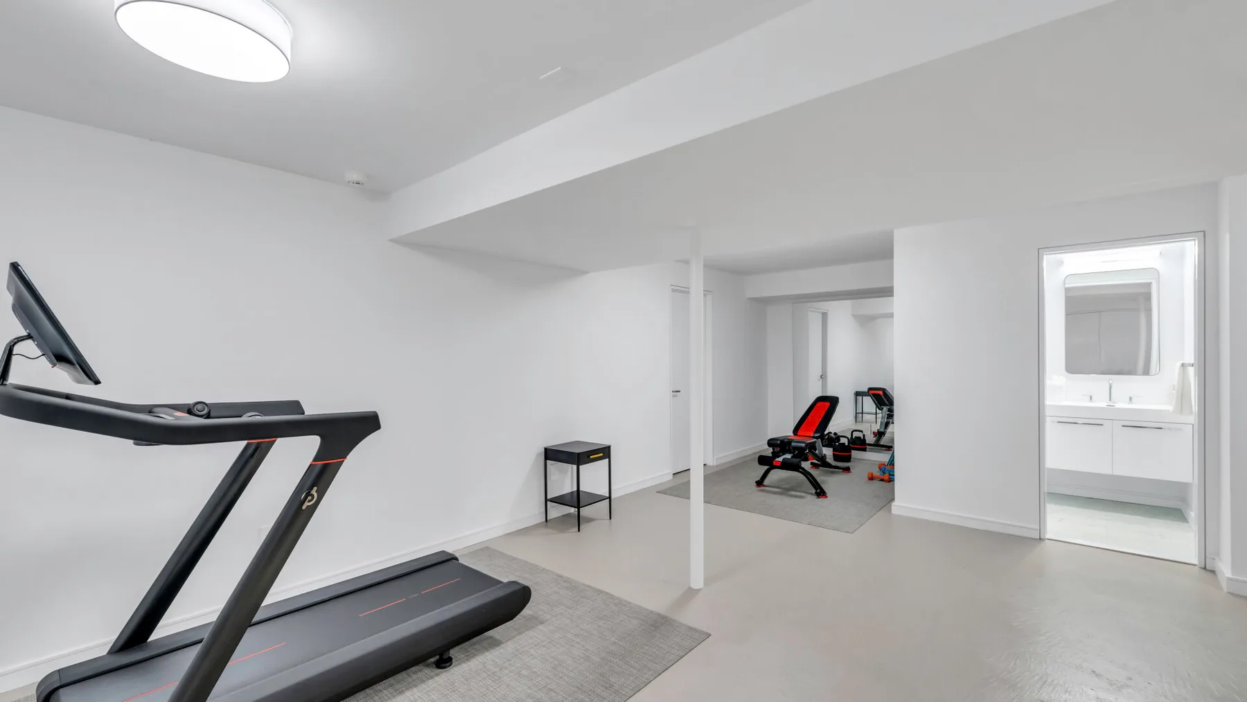 Un gimnasio en casa con equipo de ejercicio y una puerta abierta hacia un baño.
