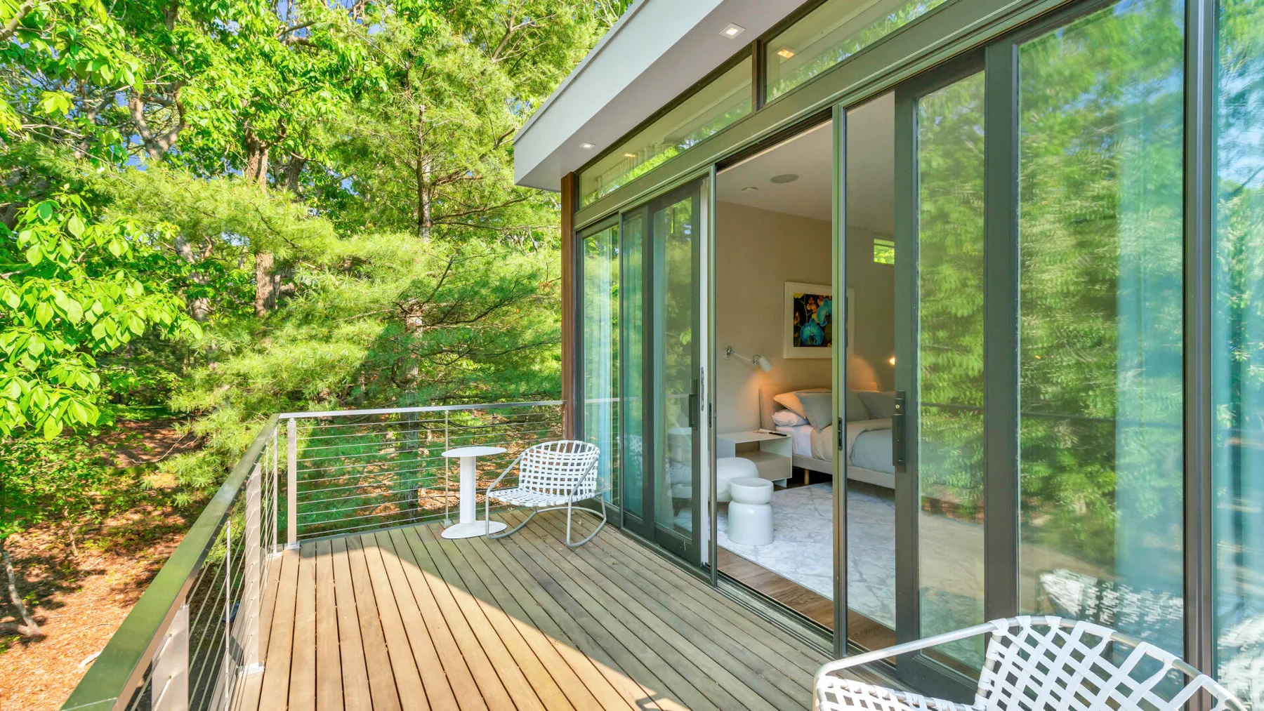 Una terraza de madera junto a una habitación acristalada, rodeada de árboles frondosos.