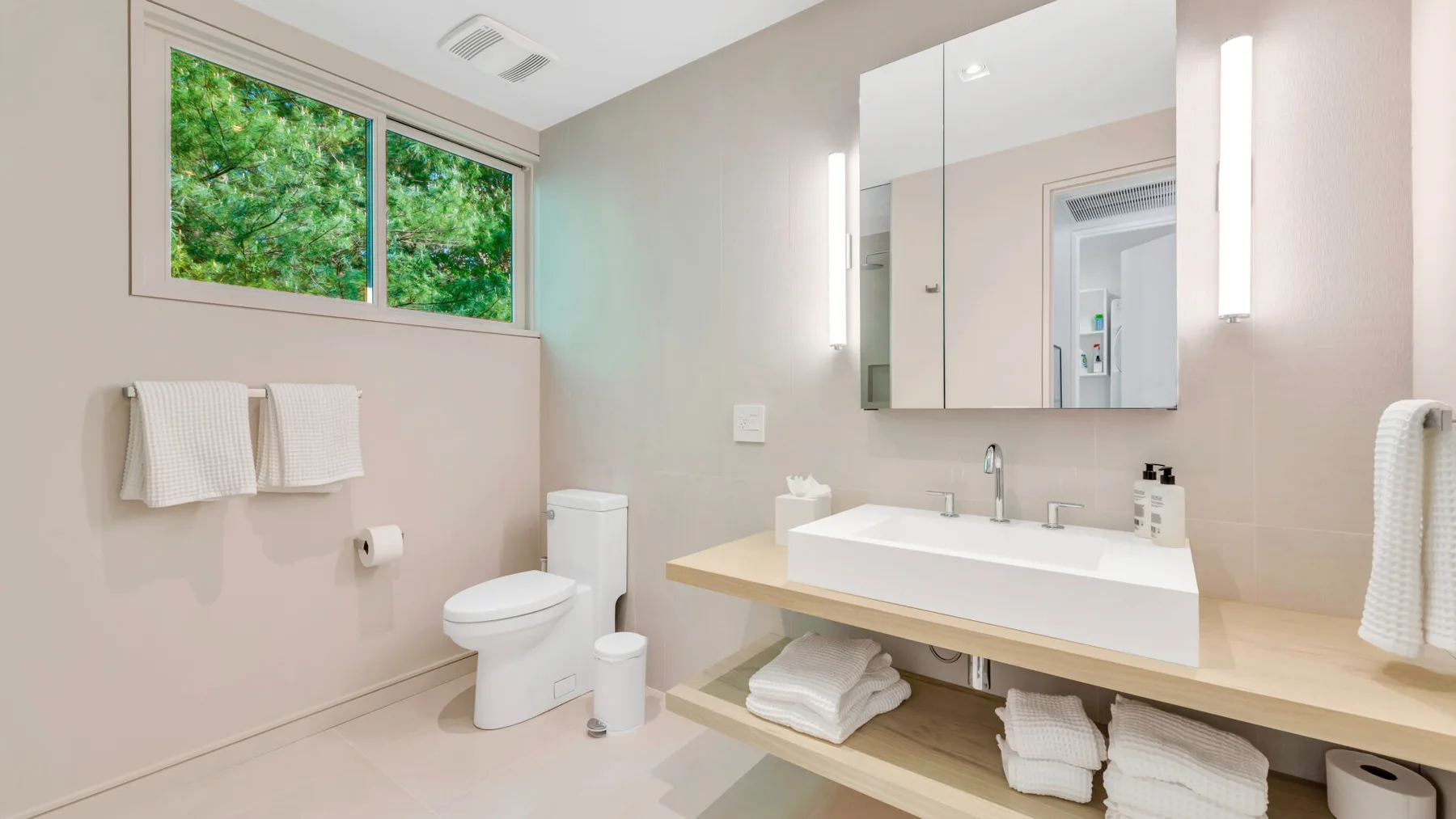 Un baño luminoso con un lavabo amplio, espejo de pared y ventana.