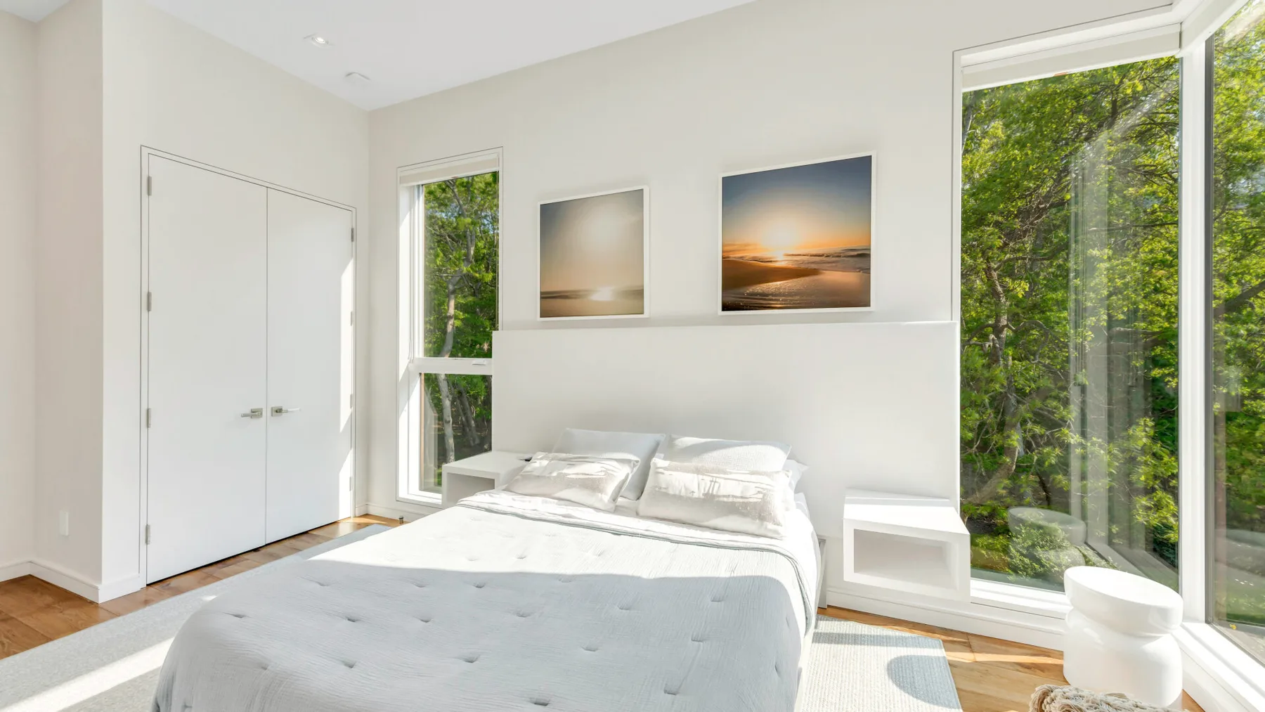 Un dormitorio luminoso con una cama junto a grandes ventanas que dan a la vegetación.