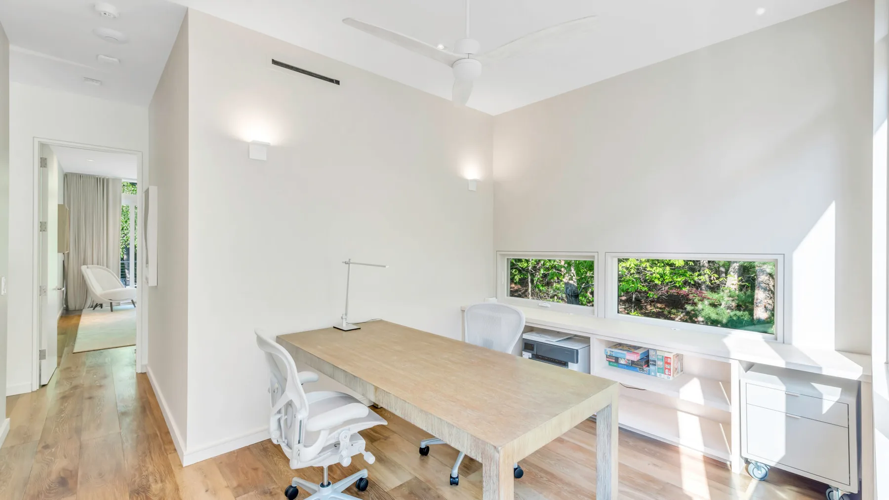 Una habitación luminosa con una mesa larga, asientos y ventanas con vistas a la vegetación.