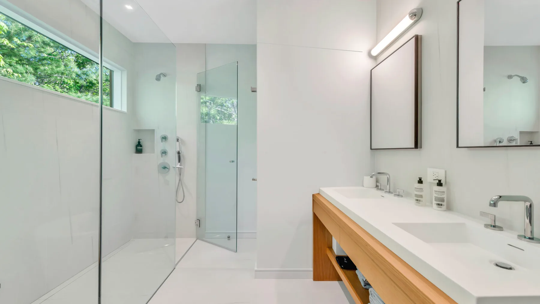 Un baño luminoso con una ducha de vidrio y un mueble de lavabo alargado.