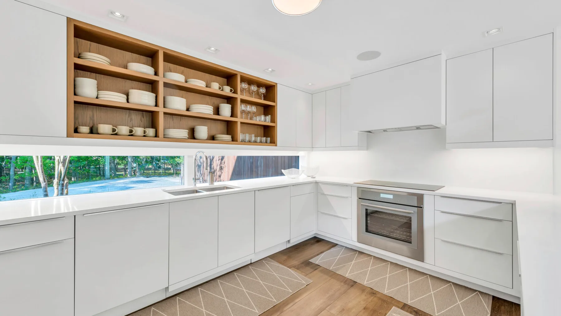Una cocina moderna y luminosa con gabinetes blancos y estantes abiertos con vajilla.