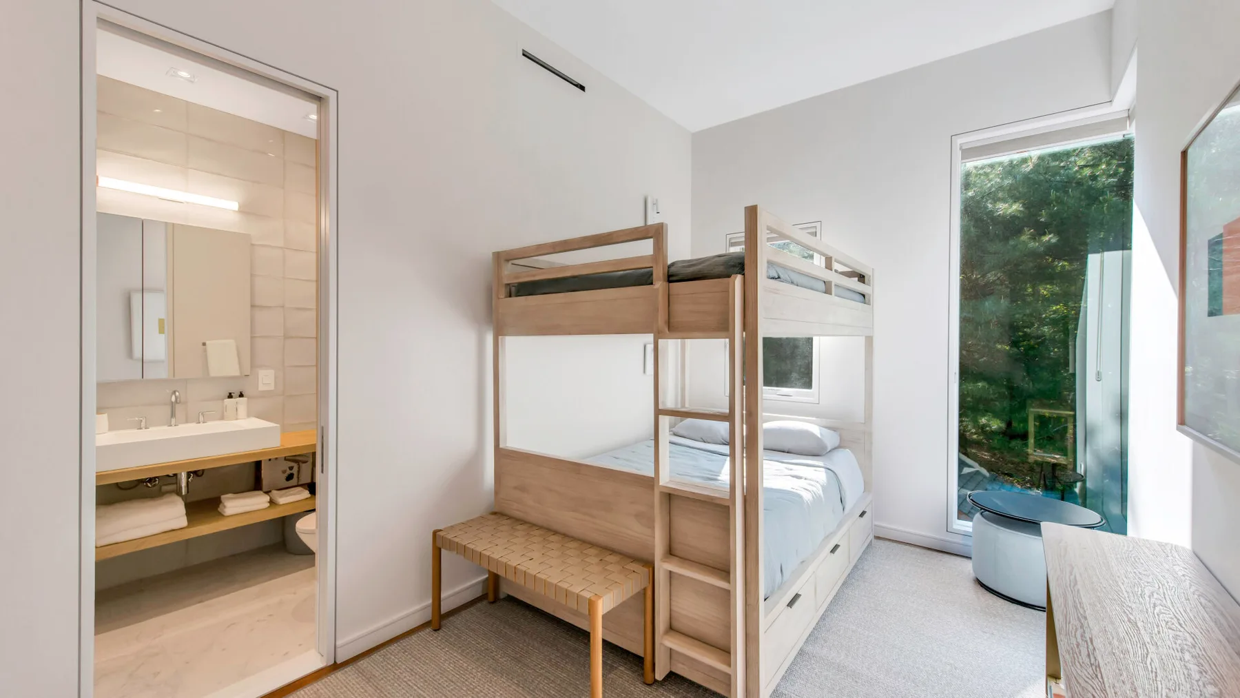 Un dormitorio luminoso con literas junto a una ventana grande con vistas a la vegetación.
