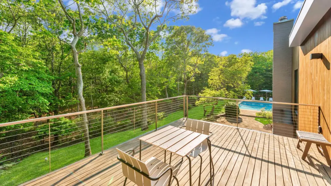 Una terraza de madera con asientos al aire libre da a un paisaje arbolado y una piscina.
