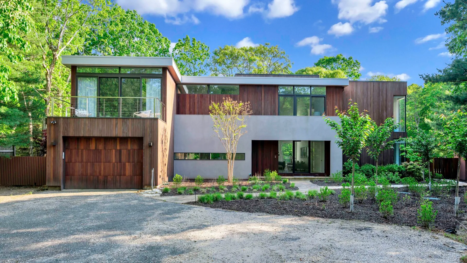 Una casa moderna con madera y ventanas de vidrio está rodeada de árboles verdes.