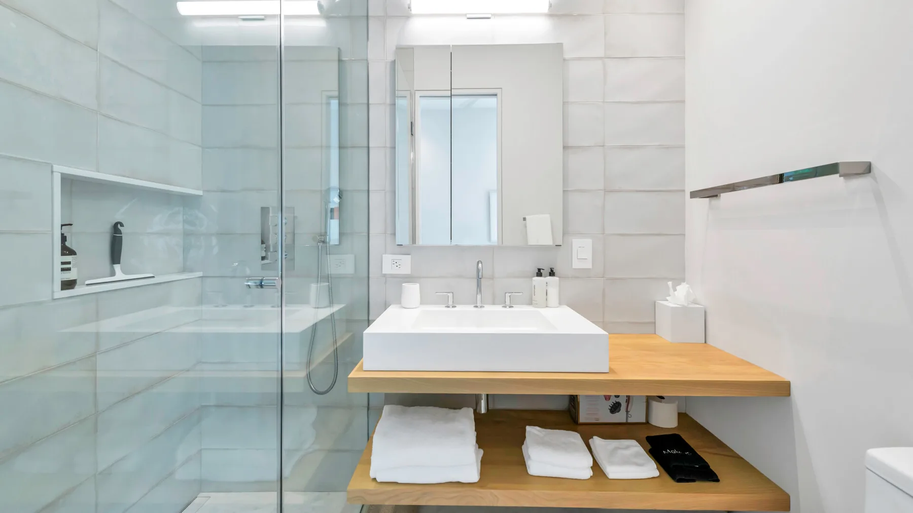 Un baño luminoso con ducha de vidrio y un lavabo sobre una encimera de madera.