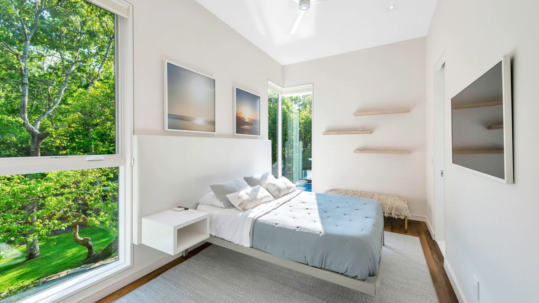 Un dormitorio luminoso con una cama junto a grandes ventanas que dan a la vegetación.