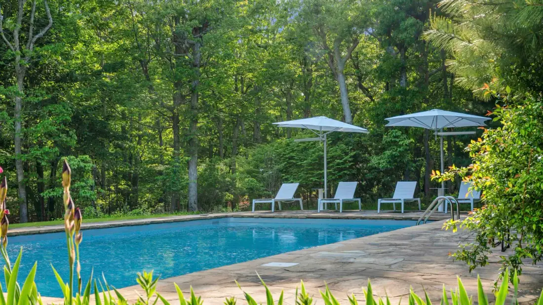 Una piscina al aire libre está rodeada de árboles y asientos junto a la piscina.