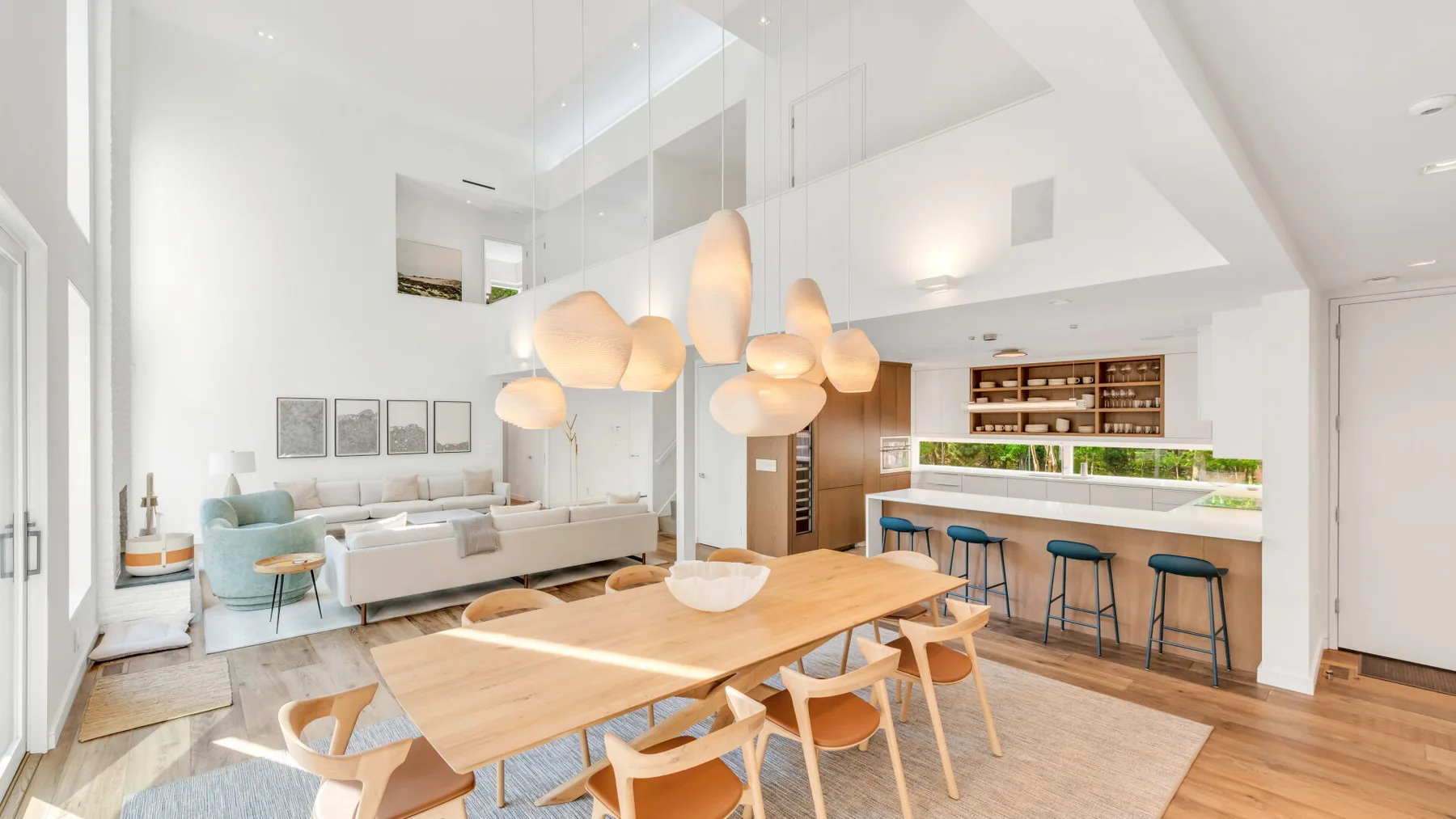 Una luminosa zona diáfana de comedor y cocina, con una larga mesa de madera y lámparas colgantes.