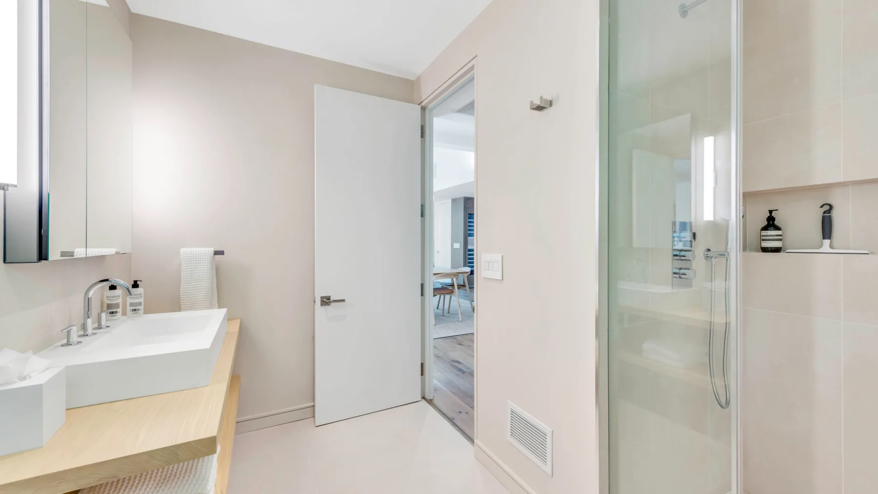 Un baño luminoso con lavabo, espejo de pared y ducha de cristal.
