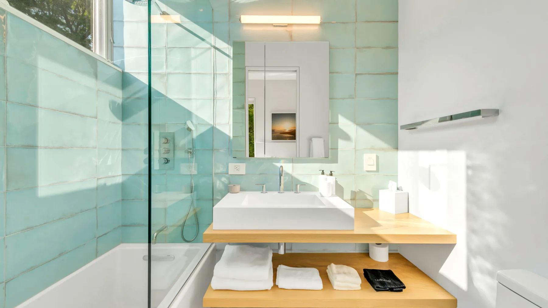 Un baño luminoso tiene una ducha de vidrio junto a un lavabo y un espejo.