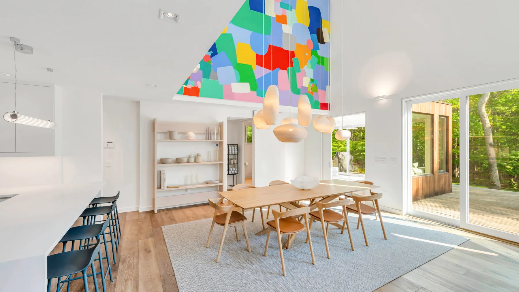 Un comedor luminoso tiene una larga mesa de madera bajo un techo con arte geométrico colorido.