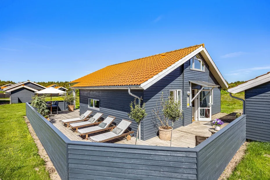 A dark-sided house with a sunny wooden deck and outdoor seating.