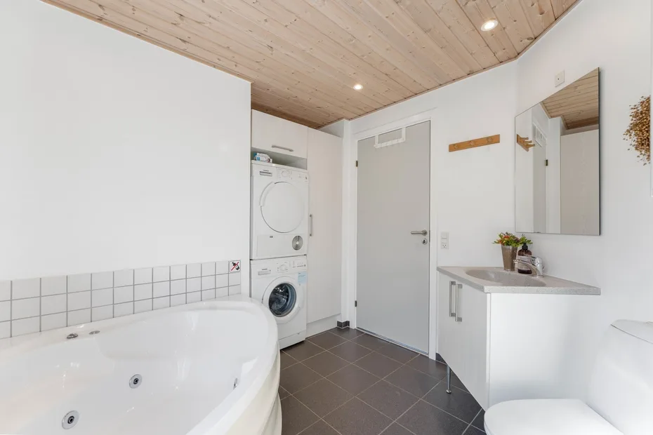 A bright bathroom with a bathtub, sink, and stacked laundry machines.