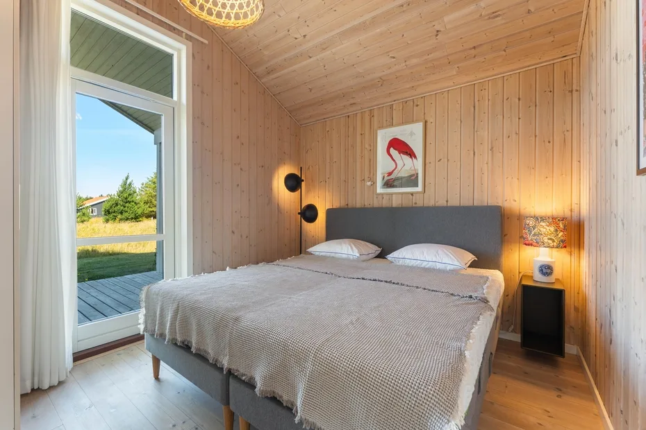 A bedroom with a double bed, bedside tables, and a glass door opening onto a deck.