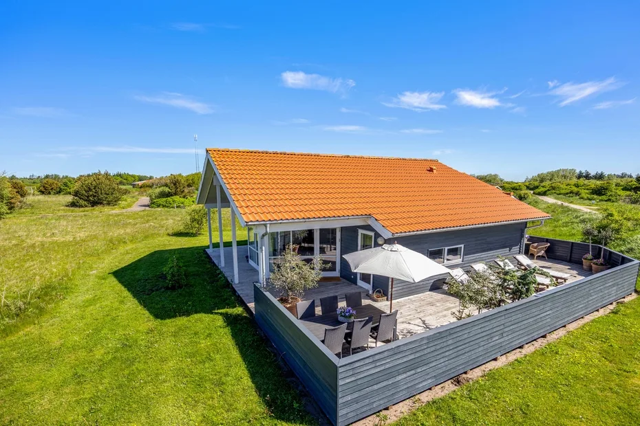 A single-story house with an orange roof sits beside an enclosed patio and open grassy land.