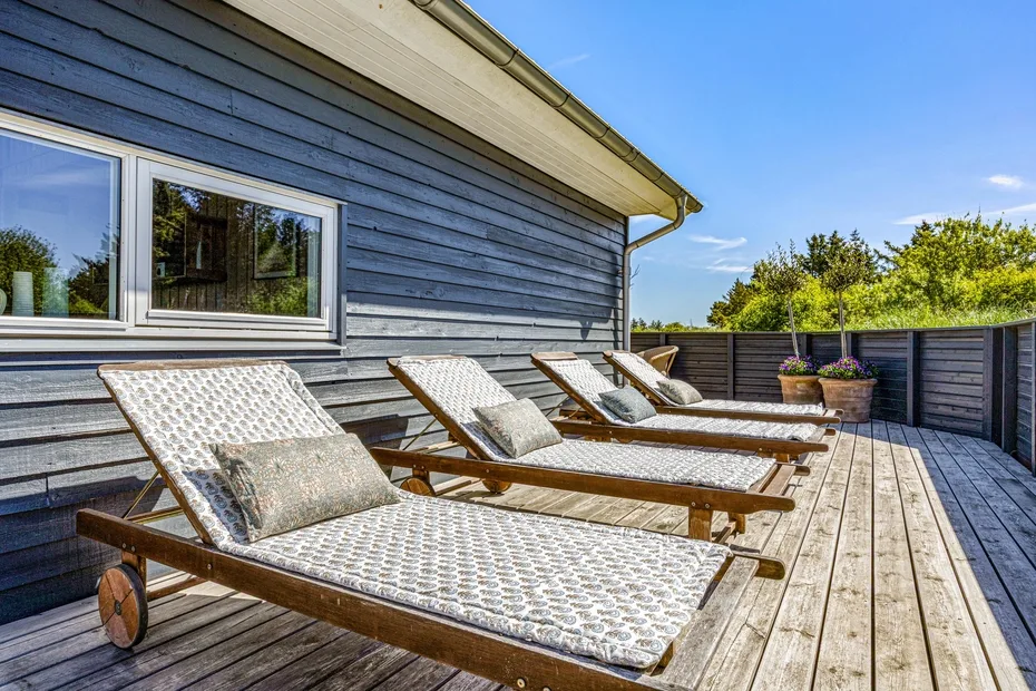 A wooden deck with reclining lounge chairs sits beside a gray-sided building.