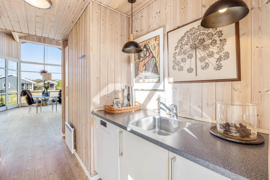 A bright kitchen with a sink and framed botanical artwork on the wood-paneled wall.